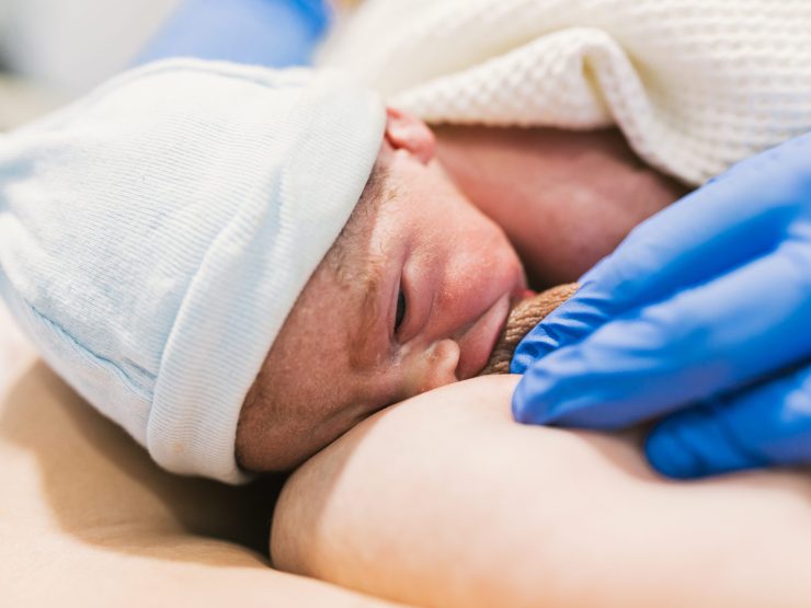 Newborn baby nursing in hospital, healthcare professional's gloved hand gently supporting.