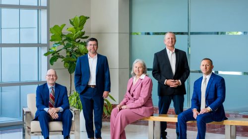 Five attorneys in professional attire, posed confidently in a modern office.
