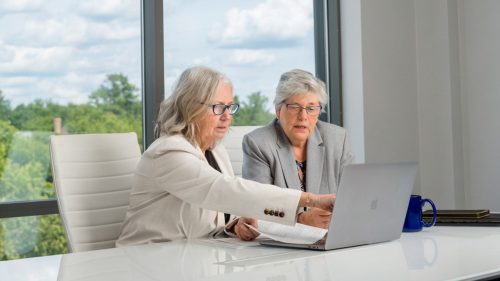 Two professionals discussing legal documents at a white desk, focused and engaged.