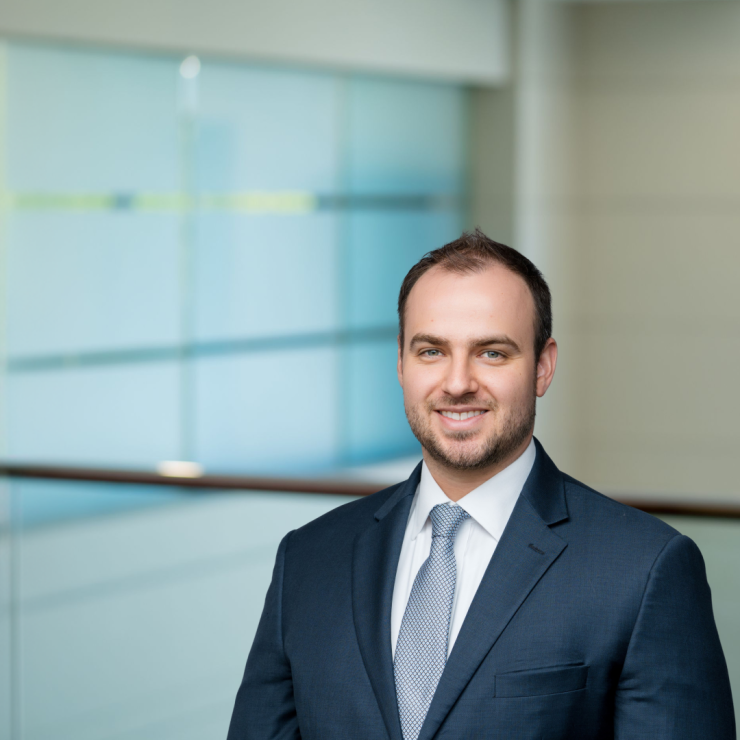 Smiling man in suit standing in modern office with glass walls.